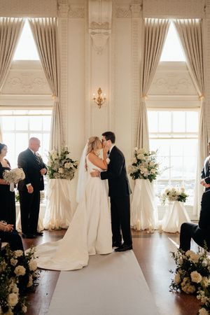 Elegant wedding ceremony sequence in a bright white ballroom with ornate architectural details and floral arrangements.