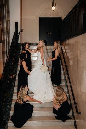Wedding party helping with dress adjustments on an elegant staircase with black railings.