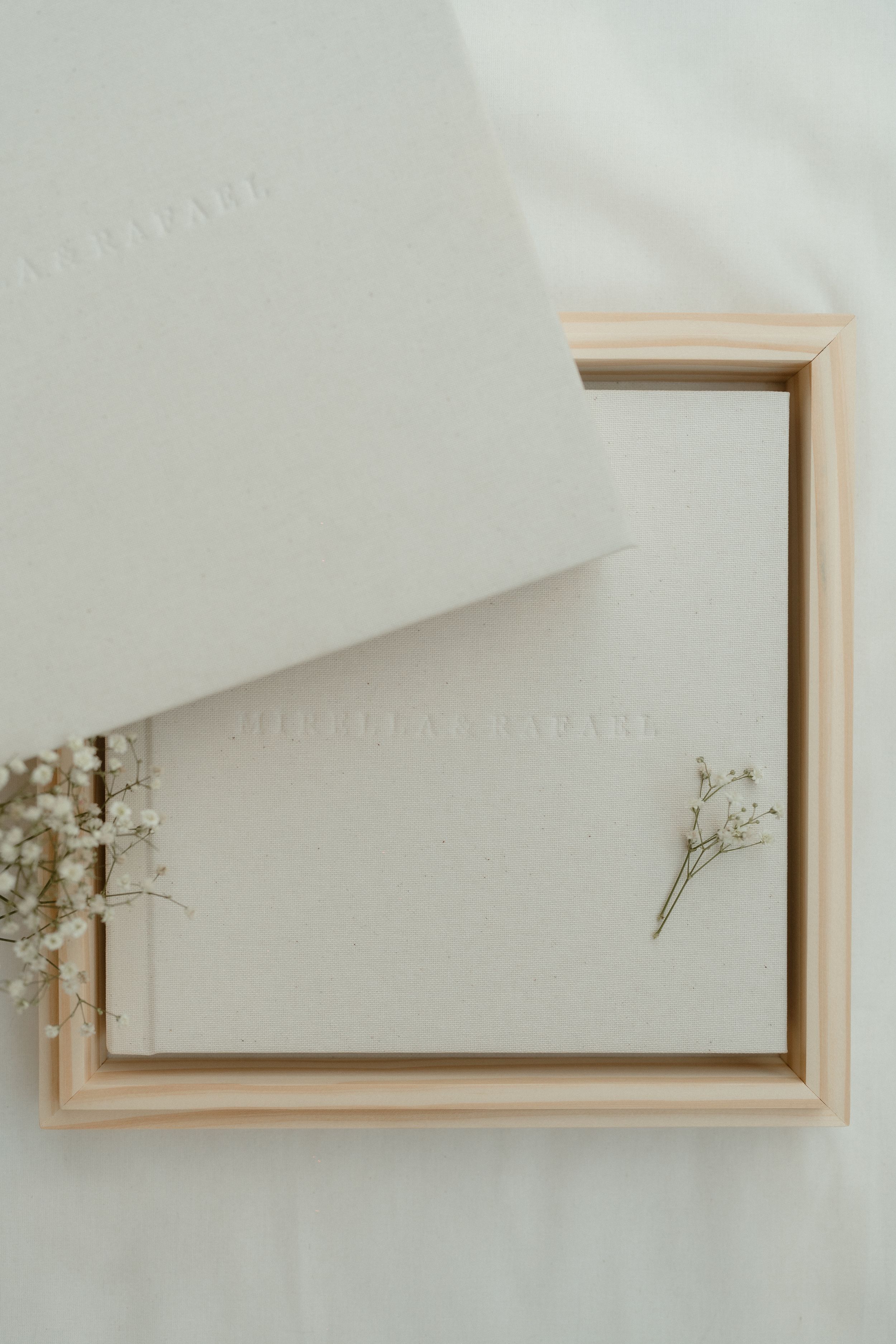 Elegant white wedding album or photo book with delicate dried flowers in a minimalist wooden box frame.