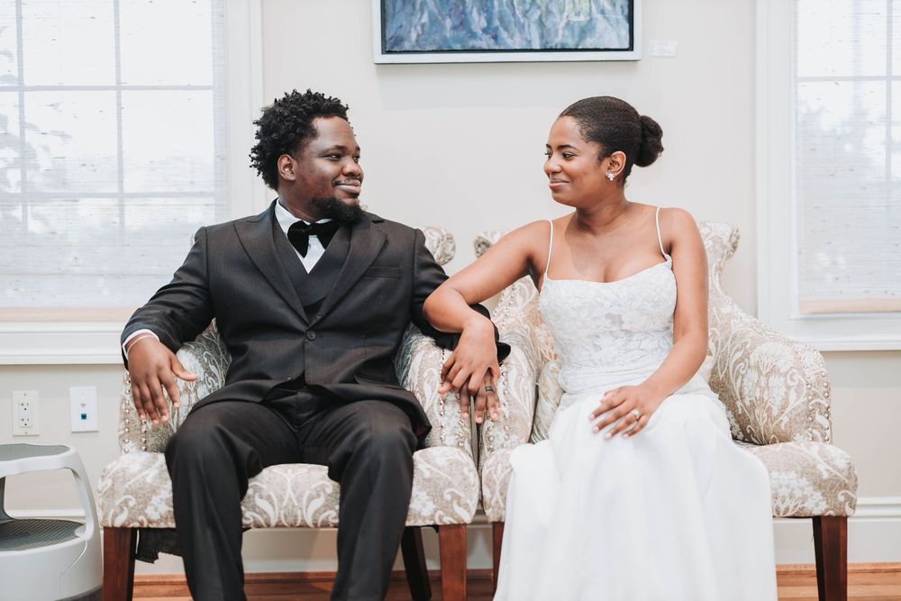 A couple shares a joyful moment while sitting together on an elegant white couch during their wedding celebration.