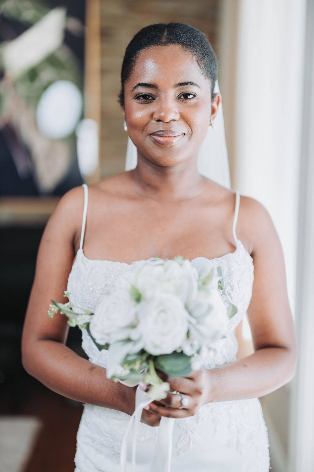 A bride holds a classic white rose bouquet while wearing a lace-detailed wedding dress with thin straps.