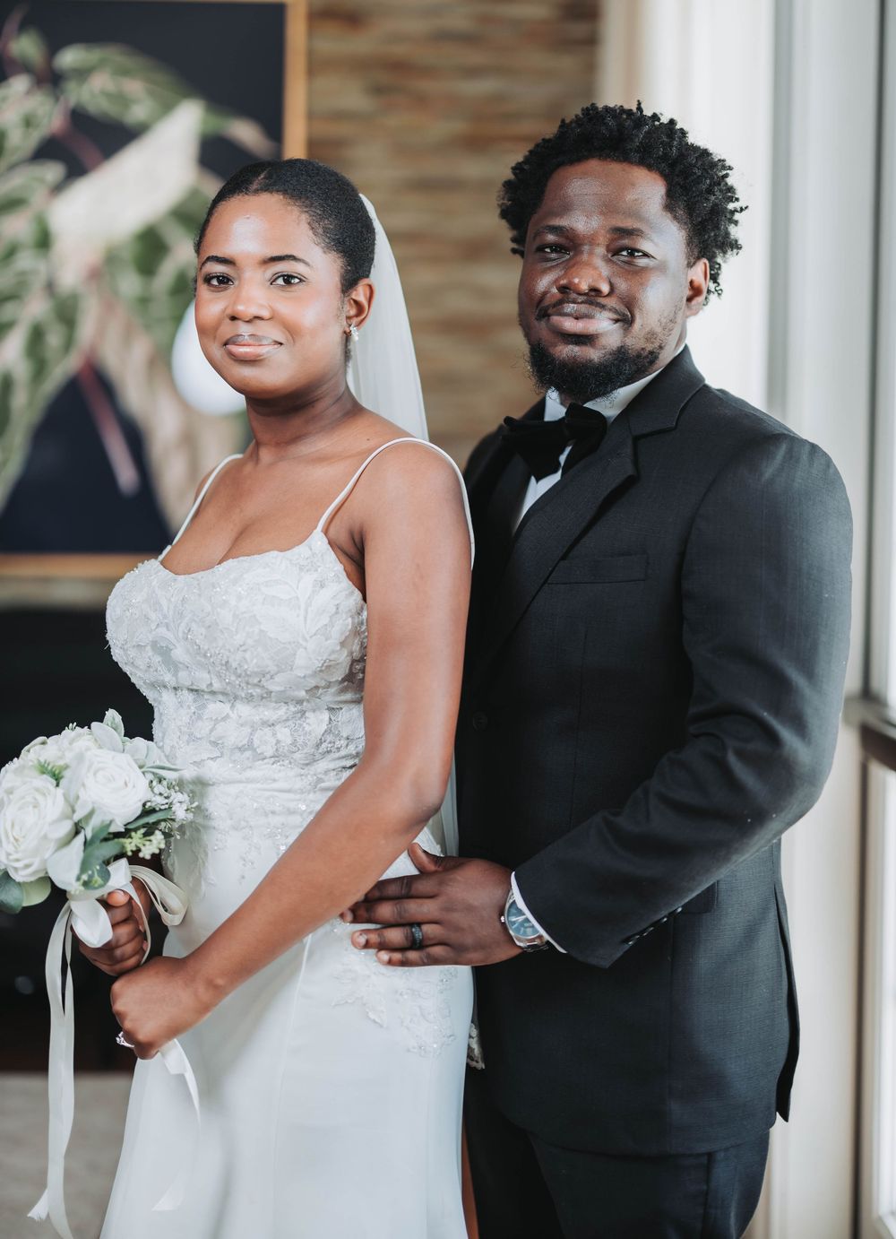 A newlywed couple poses together holding white flowers in an elegant indoor setting.