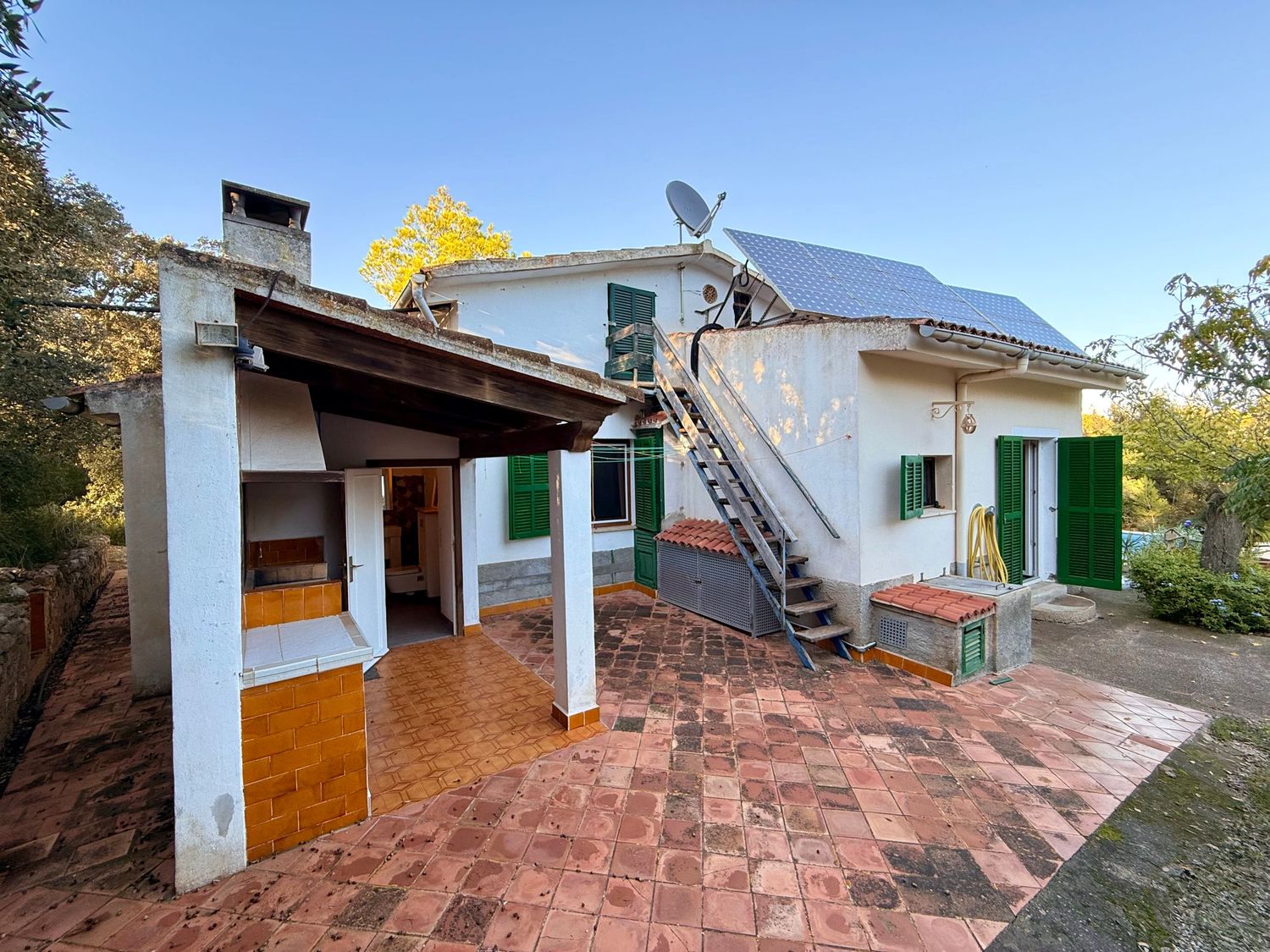 Exterior view of a rural house with white walls and green trim showing multiple angles of the terrace and roofline.