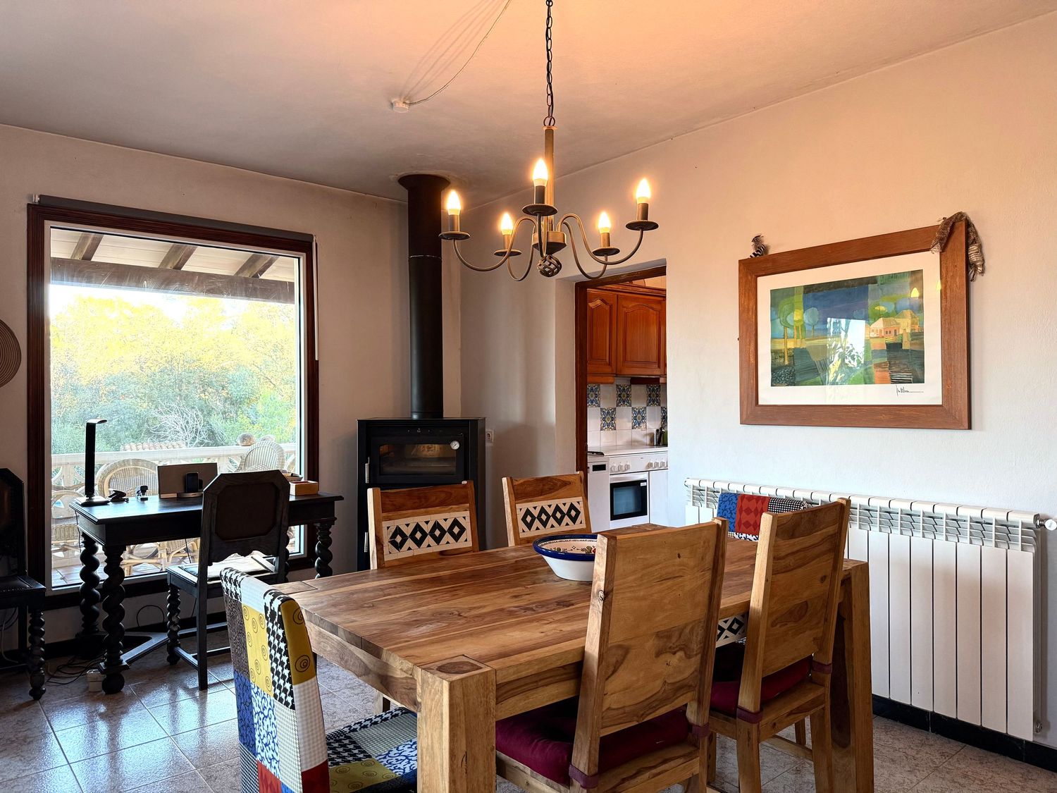 Modern dining room interior with wooden table, chandelier, and large window overlooking scenic outdoor view.