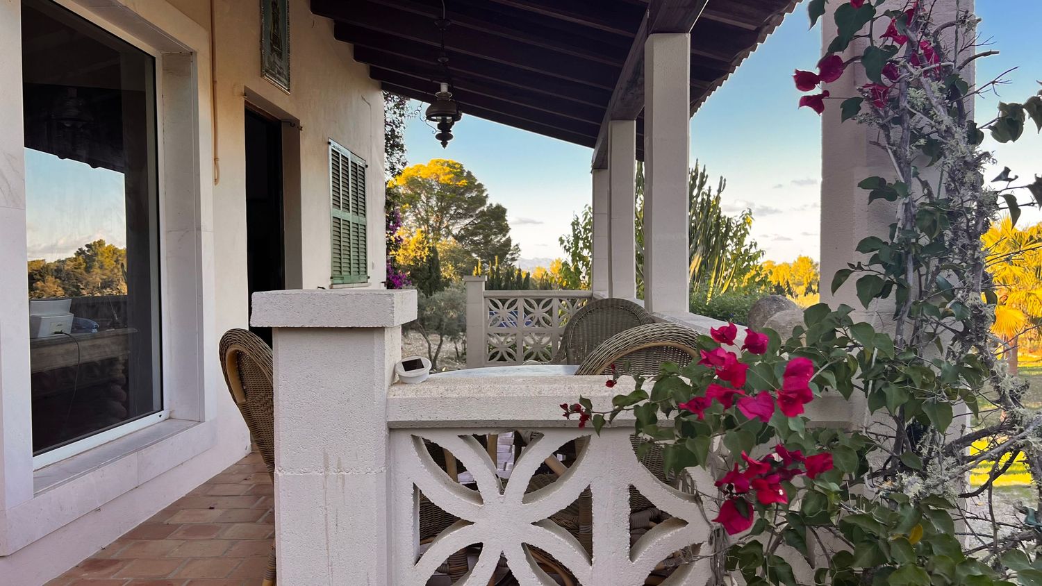 A white stucco patio with decorative columns and pink bougainvillea flowers climbing along the walls.