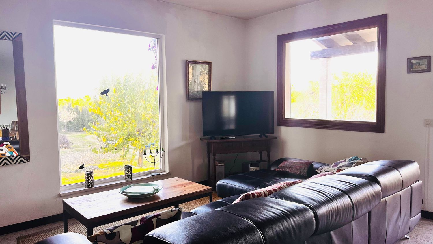 Wide angle view of a modern living room with black leather furniture and large windows letting in natural light.