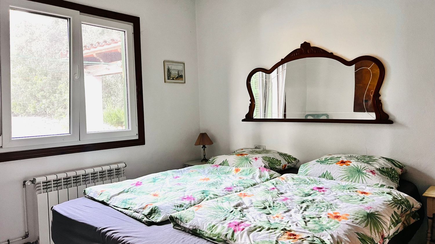 A panoramic view of a bright bedroom with white walls, floral bedding, and windows letting in natural light.
