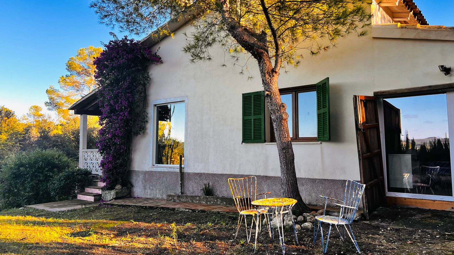 Panoramic view of a modern white villa with terrace surrounded by autumn trees and golden sunlight.