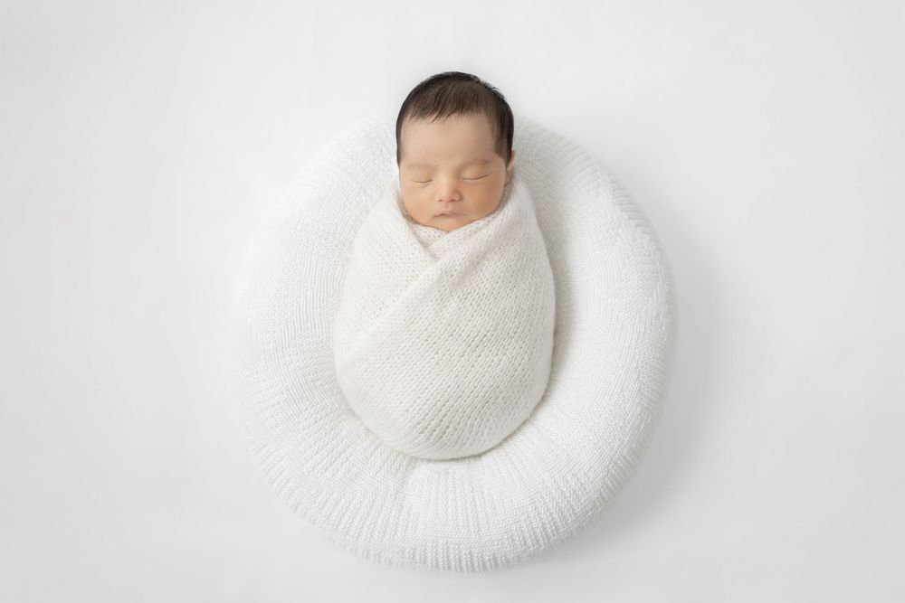 A creative photo series showing a baby wrapped in white cloth gradually disappearing into a white background.