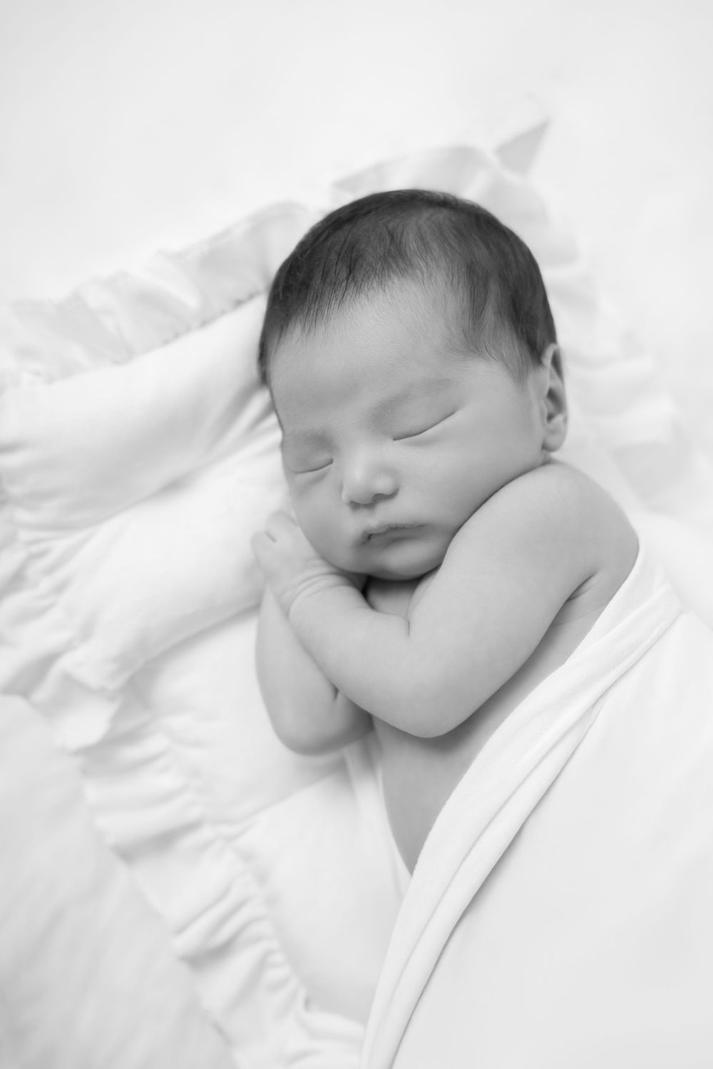 A series of peaceful black and white photos showing a sleeping newborn baby swaddled in white fabric.