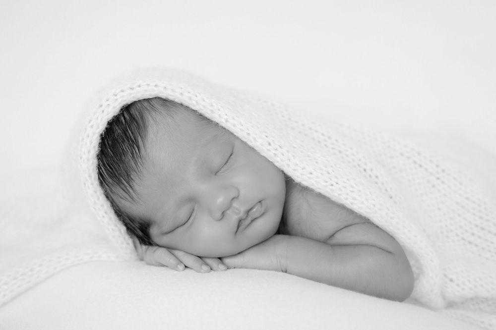 A series of peaceful black and white photographs showing a sleeping baby in different poses on soft white bedding.