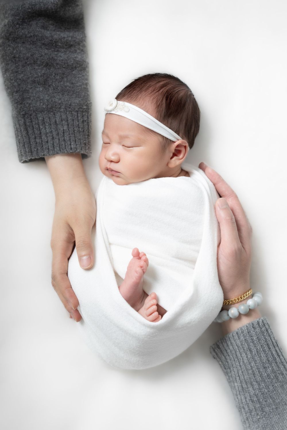 A sleeping newborn baby wrapped in white blanket with hands in grey sweater visible in multiple angles.