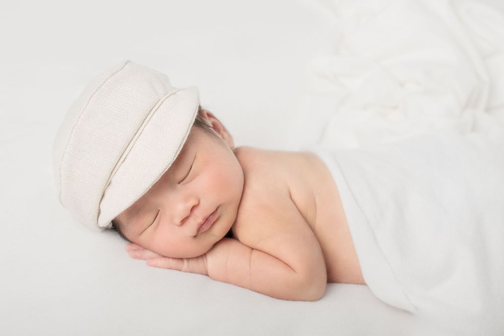 A sleeping baby wrapped in white blankets lies peacefully on a white surface.