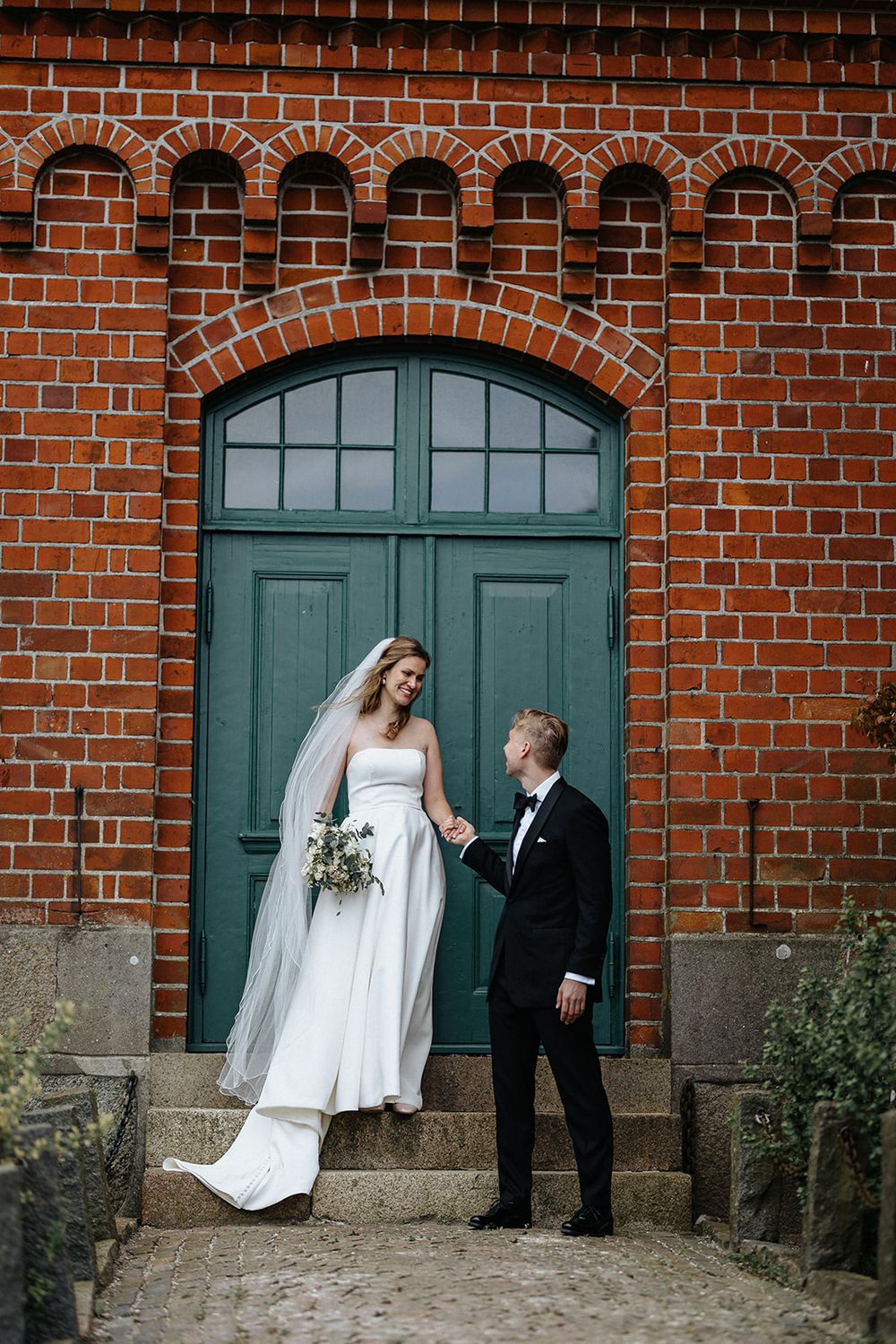 A romantic wedding photo series showing a couple posing in front of turquoise doors on a rustic brick building.