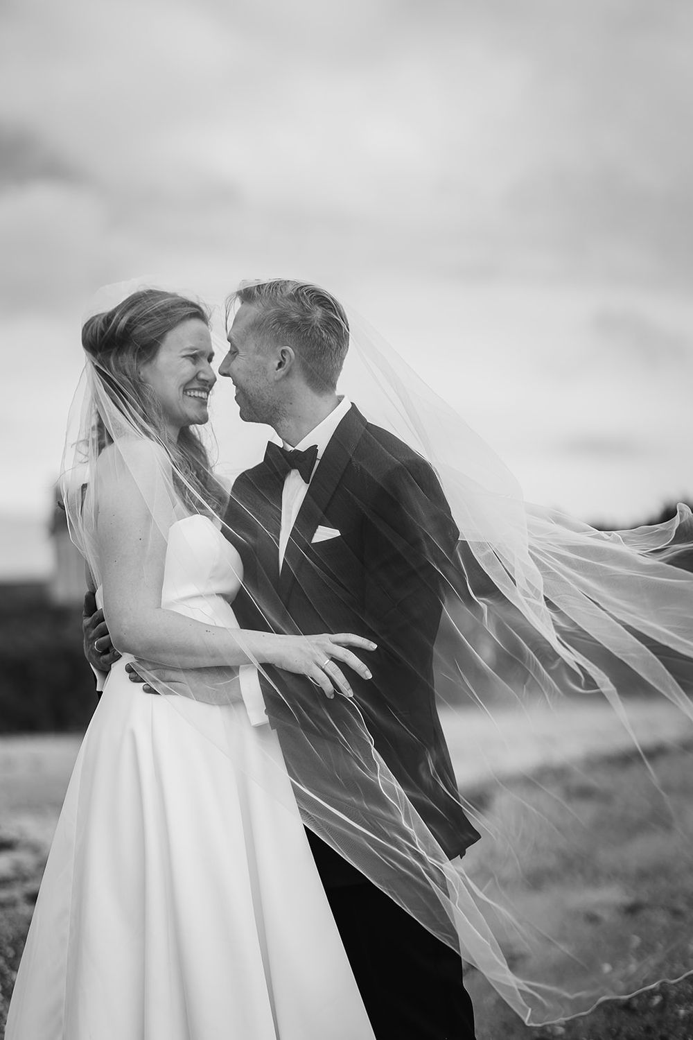 A romantic black and white wedding photo series showing a couple embracing as the bride's veil flows in the wind.