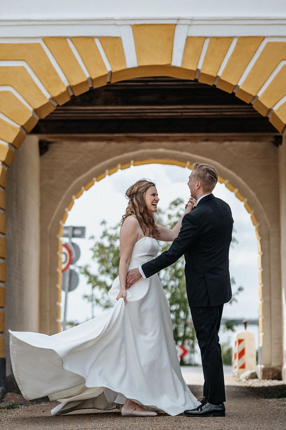 A couple shares a romantic moment under a yellow arched passageway as the bride's white dress flows in the breeze.