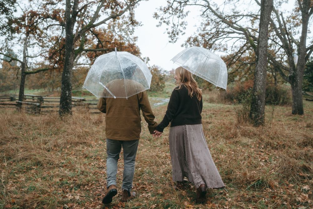 A couple holds hands while walking through a scenic autumn forest during a romantic engagement photoshoot.