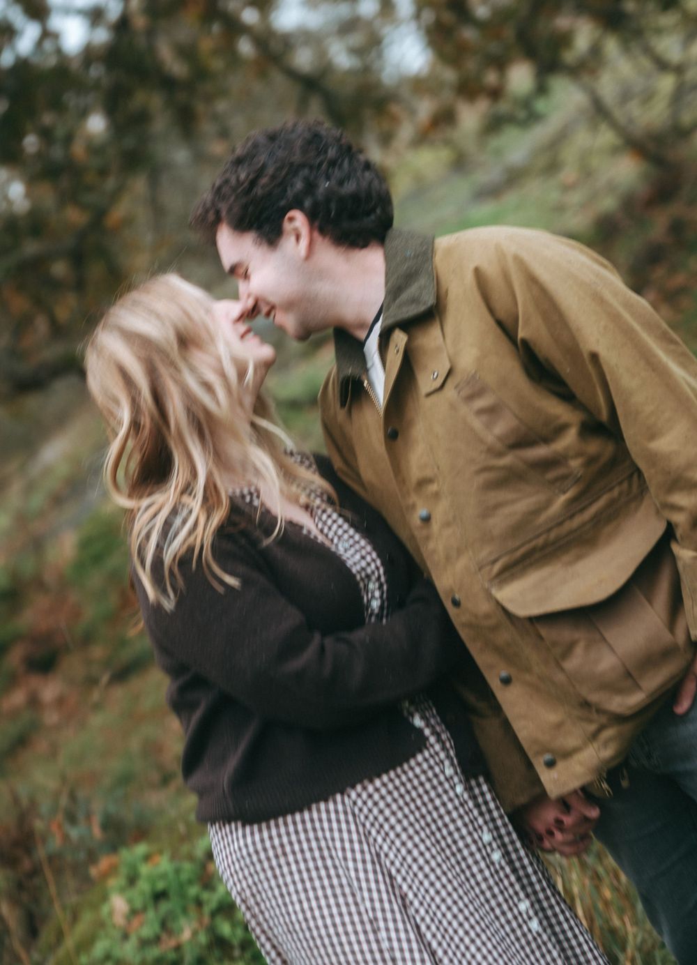 A couple shares a tender moment outdoors during autumn while wearing casual clothing.