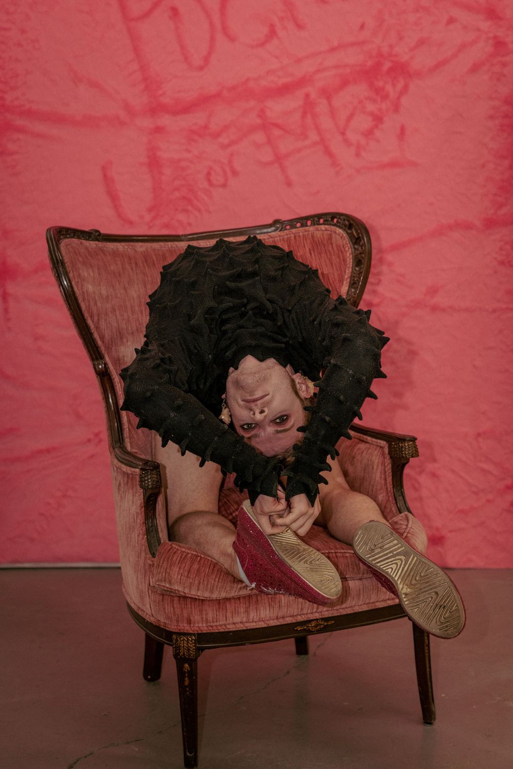 Sitting curled up in a pink chair, feet up, making playful eye contact