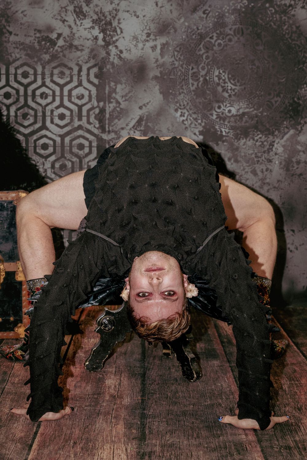 Upside-down pose with hands on the floor and intense eye contact, centered between vintage trunks