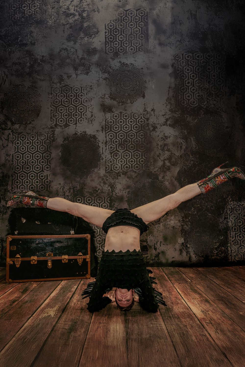 Upside-down handstand split pose on wood floor with black and gray backdrop
