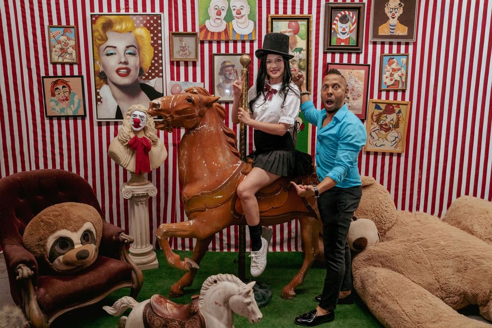Sitting on the carnival horse with arms around a friend, surrounded by whimsical props