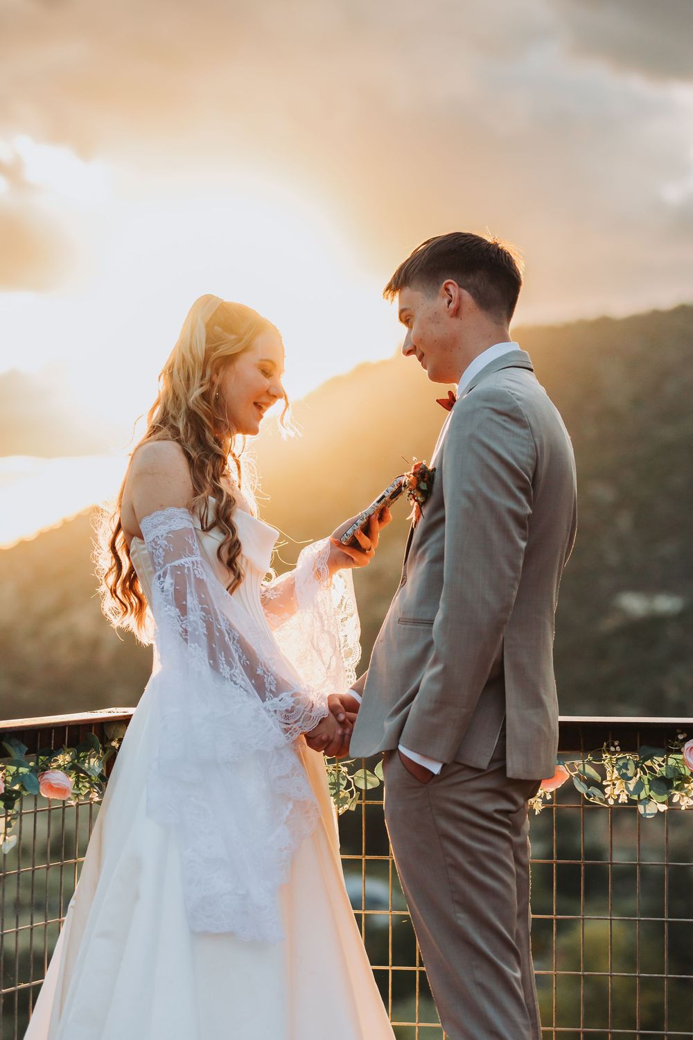 Newlywed couple shares intimate moment at sunset on balcony with mountains in background.