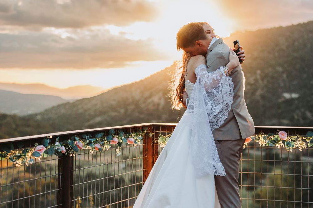 Newlywed couple embraces during golden mountain sunset with scenic valley views in background.