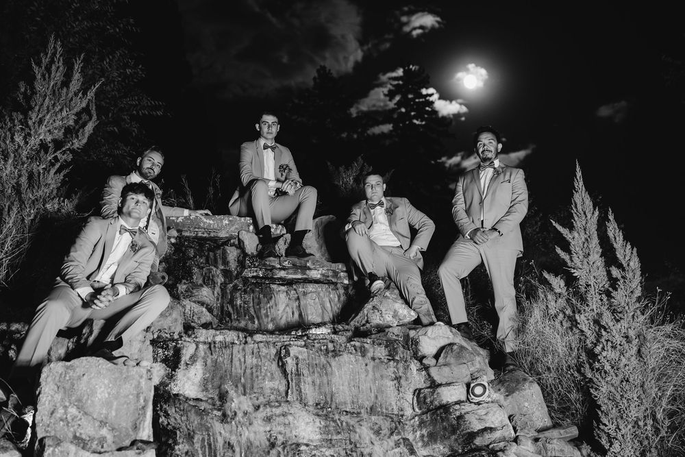 A group of people sit on rocks at night with the moon illuminating the desert landscape in black and white.