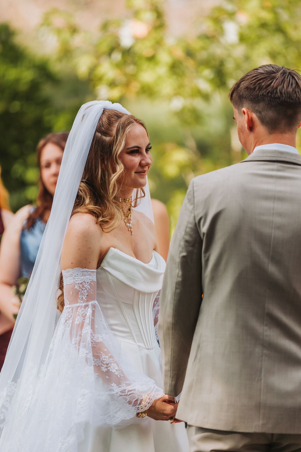A bride in a white lace gown and veil shares an intimate moment during an outdoor garden wedding ceremony.