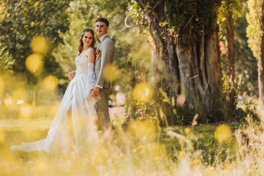 Romantic couple embraces in golden sunlit meadow surrounded by blurred yellow wildflowers and trees.