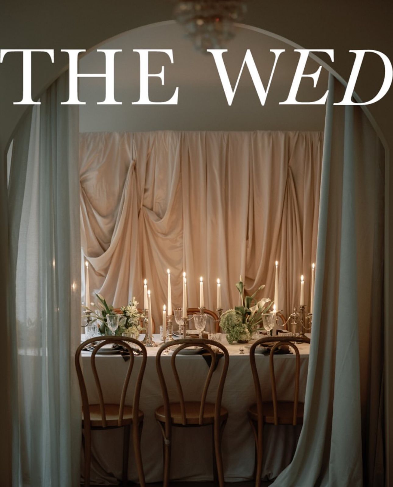 Elegant wedding reception table setup with white candles and floral centerpieces in a dimly lit room with draped curtains.