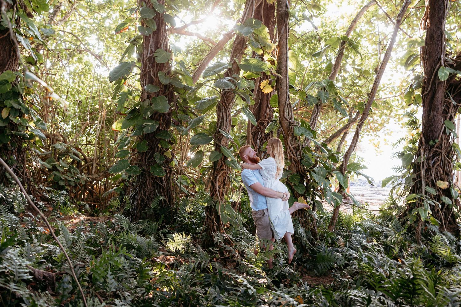 A person walks through a lush forest path surrounded by dense tropical vegetation and tall trees.