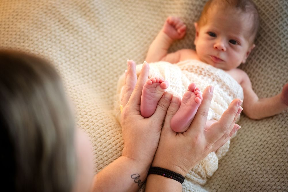 A mother tenderly holds her newborn baby's tiny feet while the infant lies on a soft blanket.