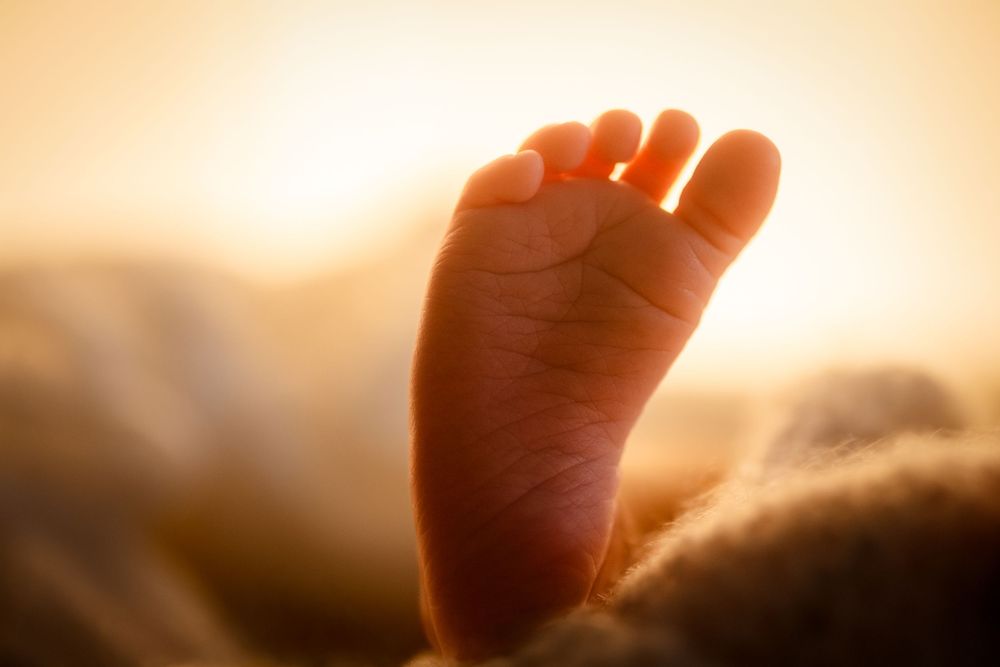 Close-up of a newborn baby foot glowing in warm golden sunset light, soft and delicate skin detail.