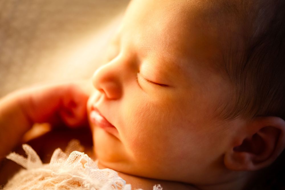 Close-up of a peacefully sleeping newborn baby bathed in warm golden sunlight.