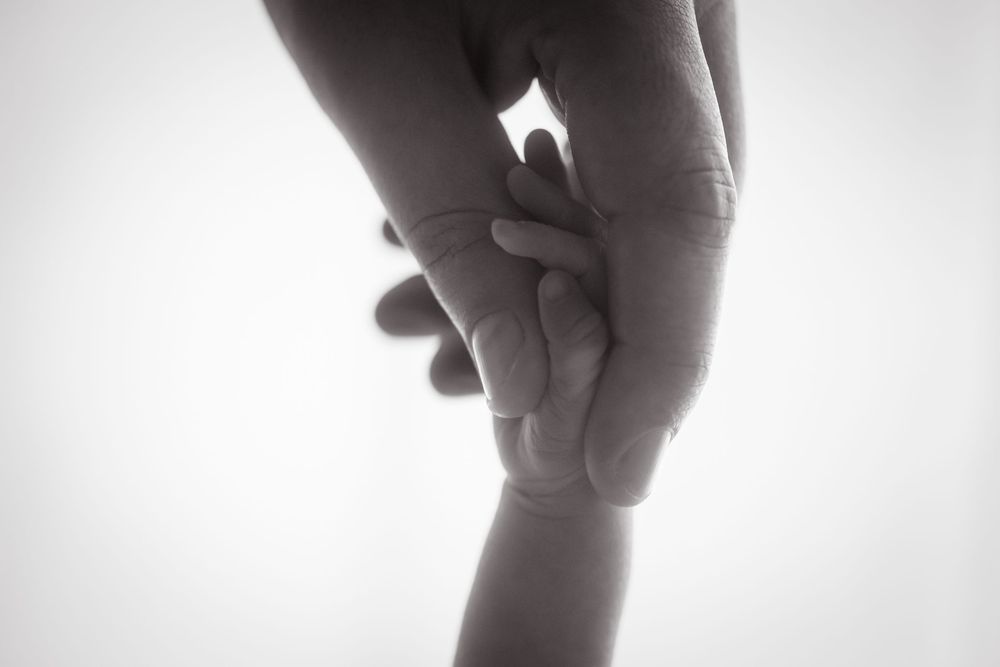 Black and white photo of an adult hand gently holding a small baby's hand, symbolizing love and parental bond.