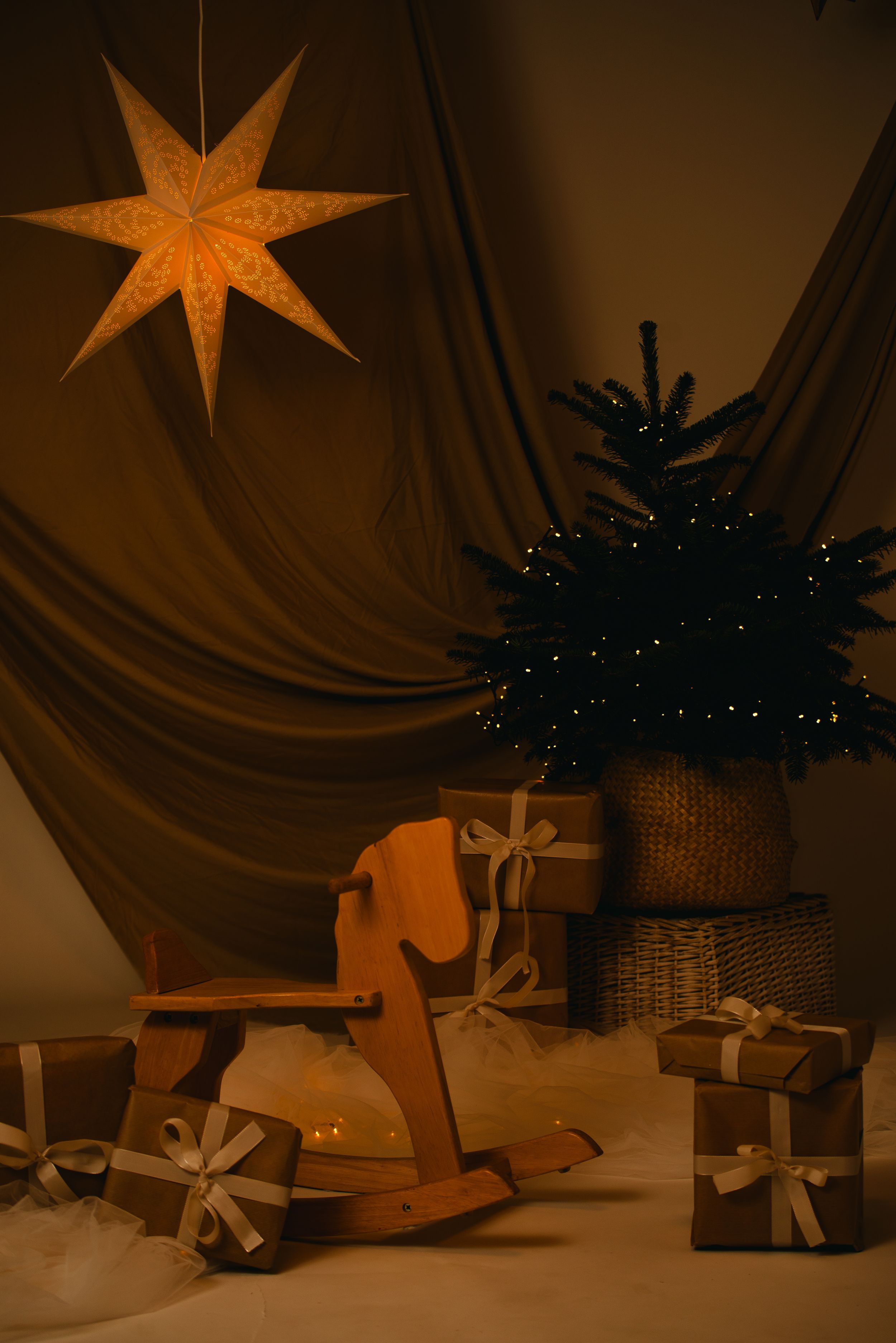 Decorative paper star lanterns and wrapped presents create a cozy holiday scene with warm lighting and shadows.