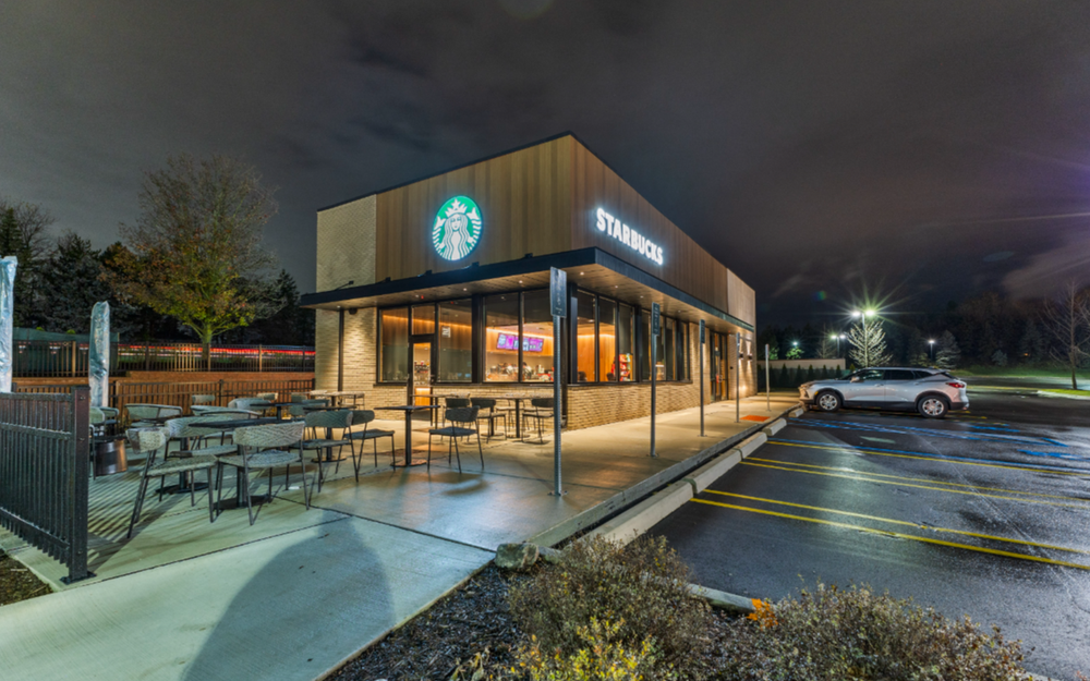 Starbucks standalone building exterior at night with lit signage, outdoor seating, and parking lot.