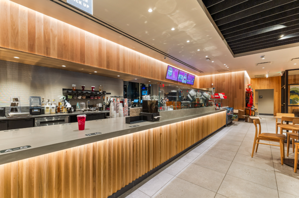 Modern Starbucks counter with wood paneling, espresso machines, ambient lighting, and tiled flooring.