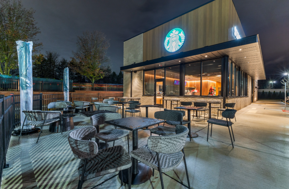 Starbucks outdoor patio at night with black chairs, tables, and illuminated storefront signage.