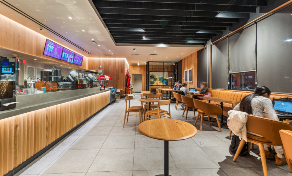 Starbucks interior at night with customers seated, wood-paneled counter, and glowing digital menu boards.