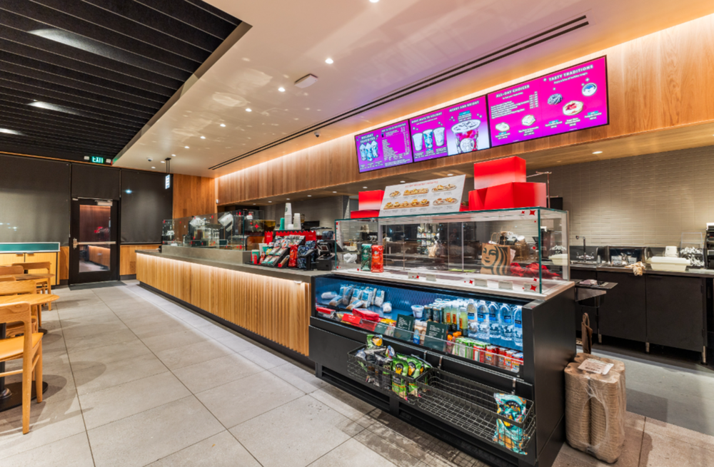 Starbucks service counter with digital menu boards, refrigerated grab-and-go case, and espresso equipment.