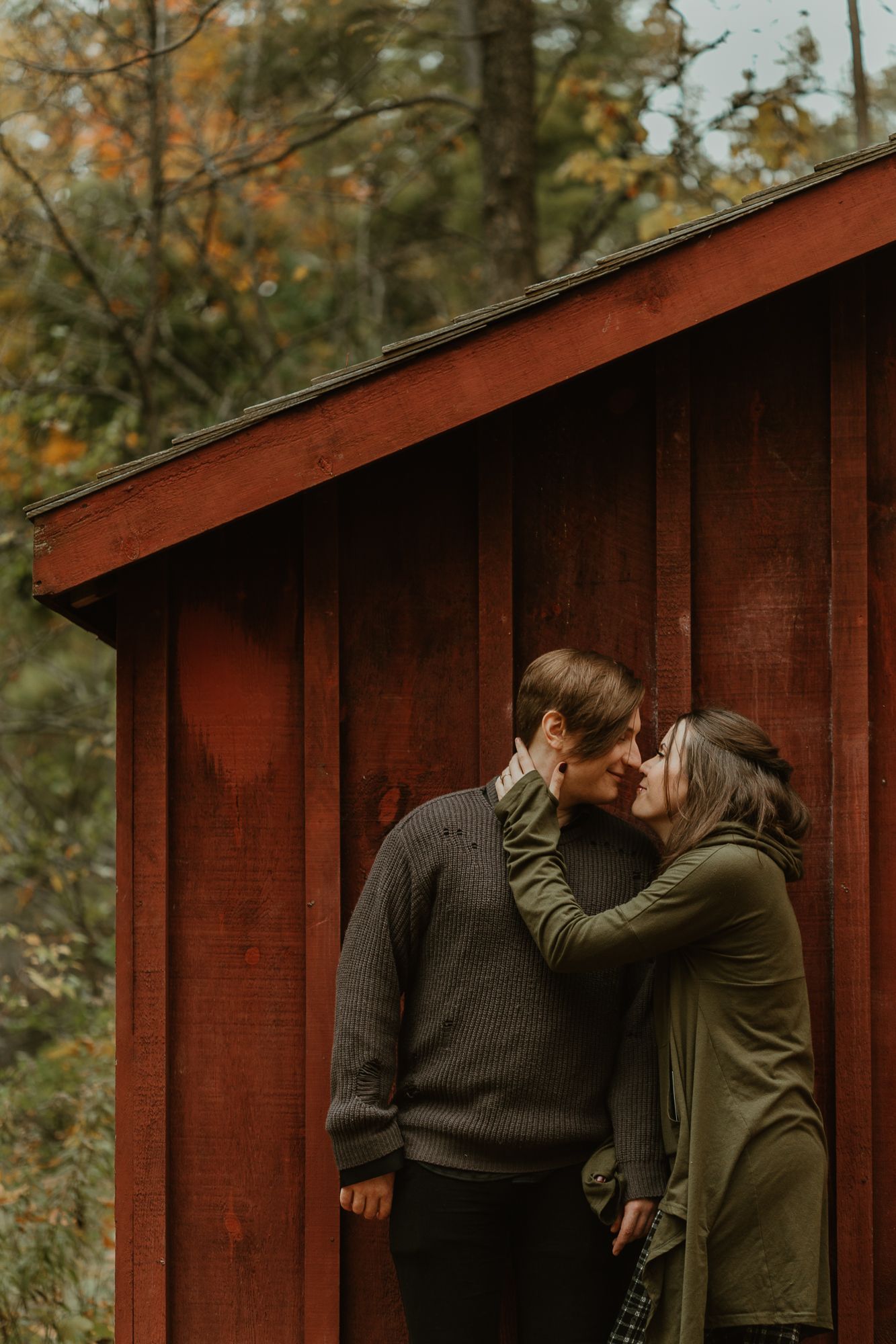 A romantic autumn scene shows a couple sharing tender moments against a rustic red barn wall in nature.