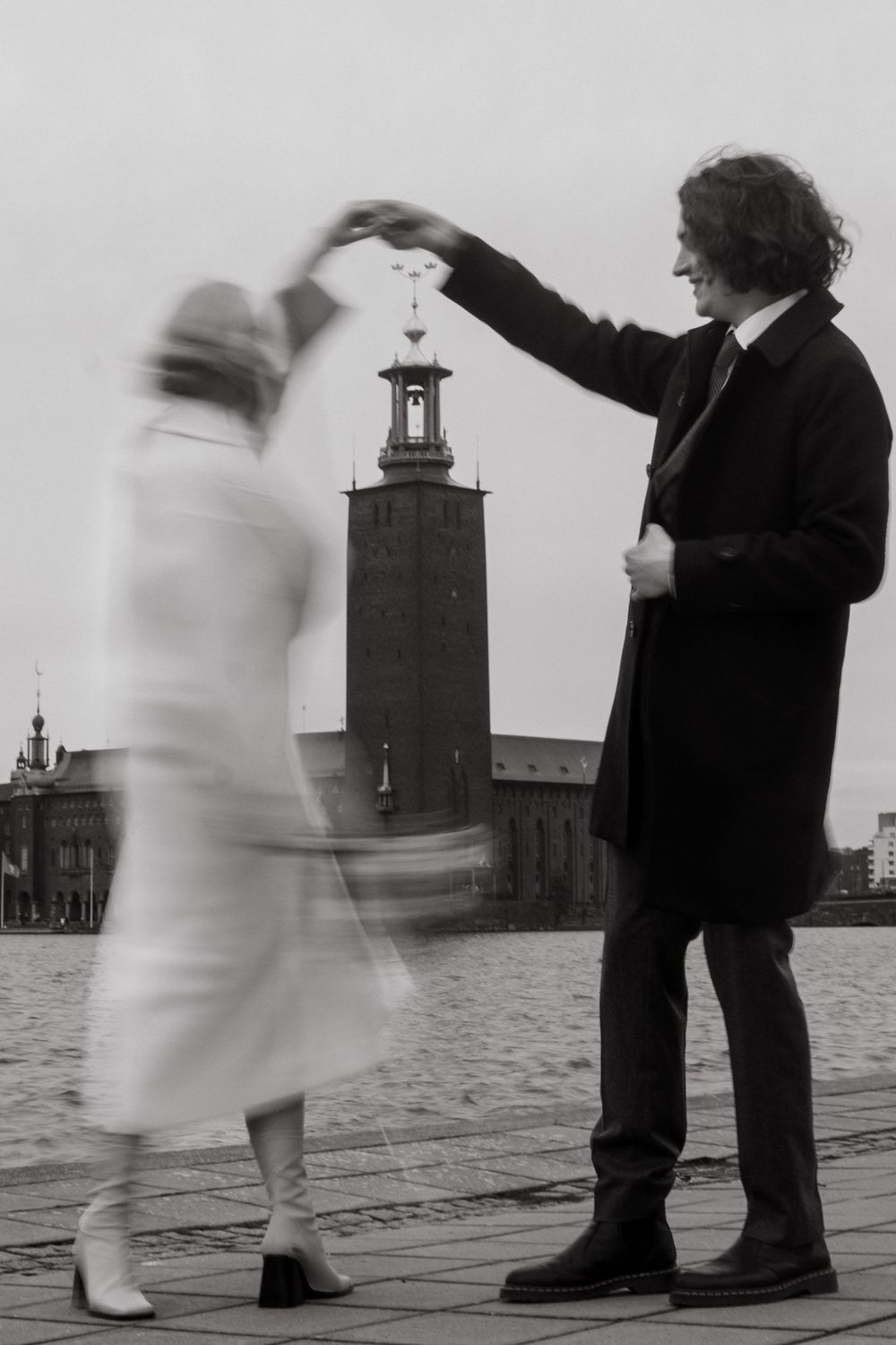 man spinning his wife around with Stockholm City Hall in the background while being captured by cinematic wedding photographer in Stockholm