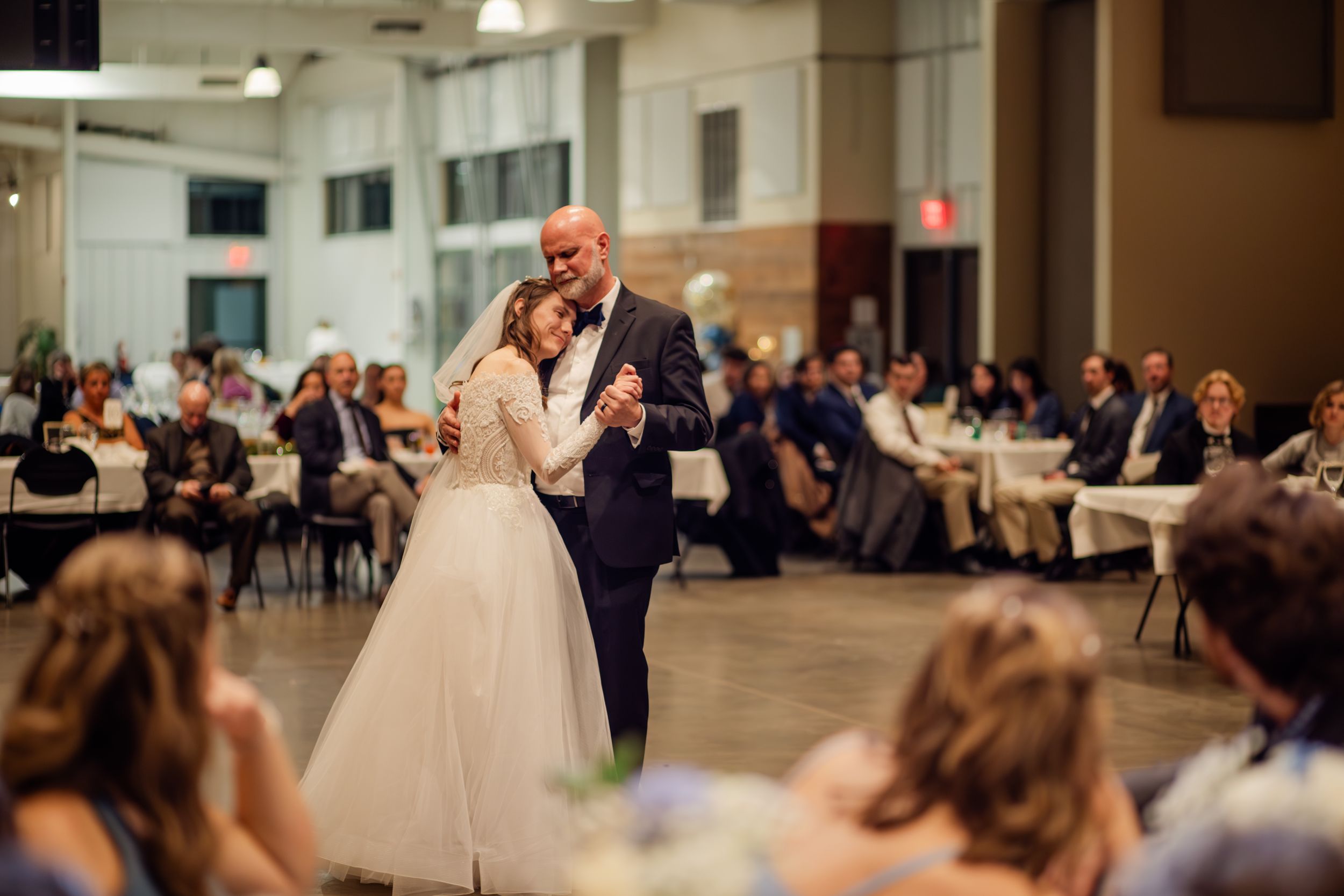 A couple shares their first dance at a wedding reception while guests watch and take photos with their phones.