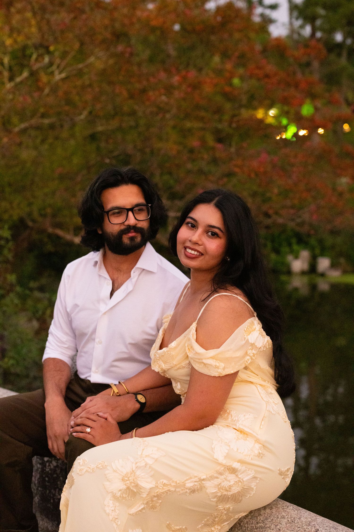 Couple sits together by a pond in a colorful Japanese autumn garden.