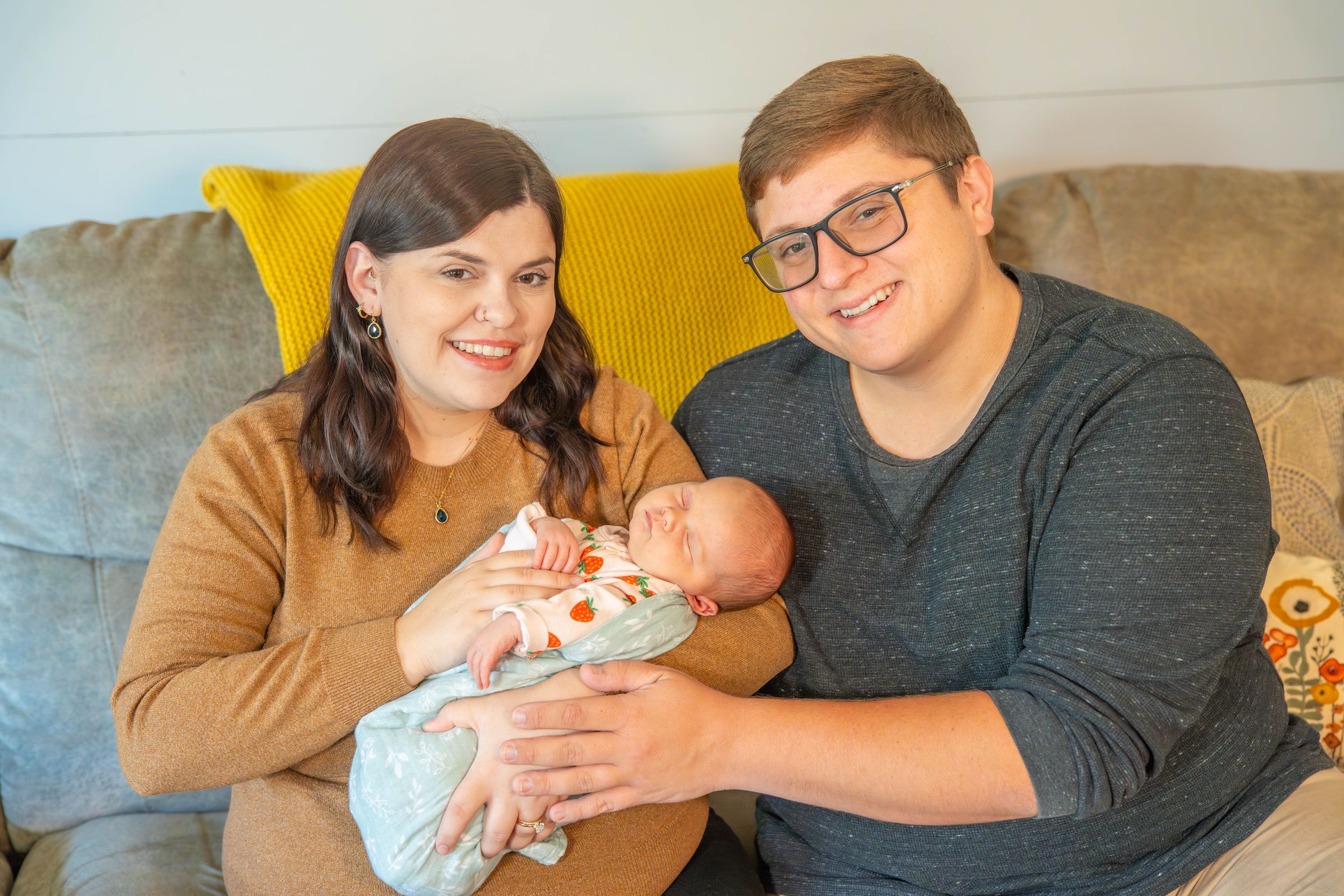 A couple sits on a couch holding and gazing lovingly at their newborn baby in a series of tender moments.