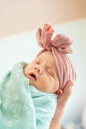 A sleeping newborn baby wearing a pink headband and mint green swaddle blanket in a series of peaceful portraits.
