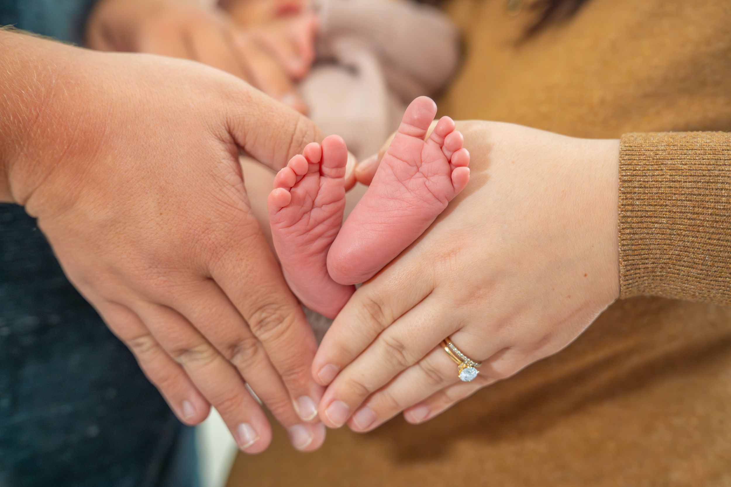Close-up shots of gentle hands holding tiny newborn baby feet and fingers against a warm-toned background.